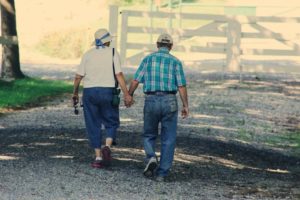 couple de seniors qui se tiennent la main en se baladant dans la campagne