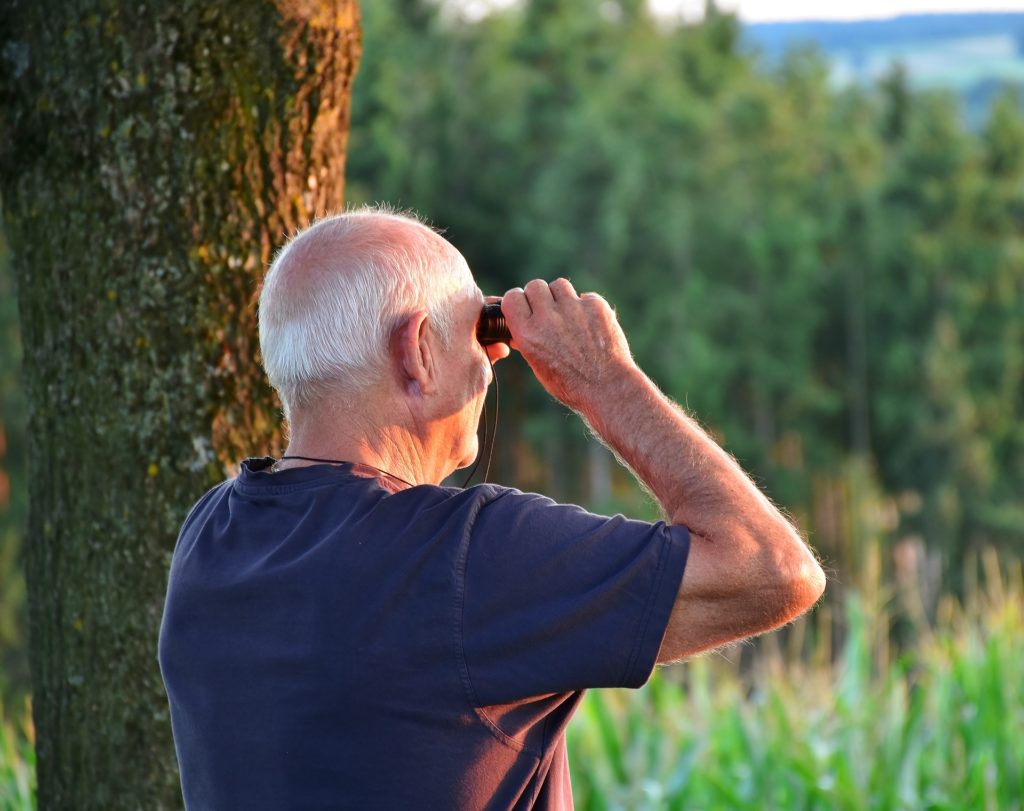 Homme âgé seul qui regarde au loin avec des jumelles dans la nature 