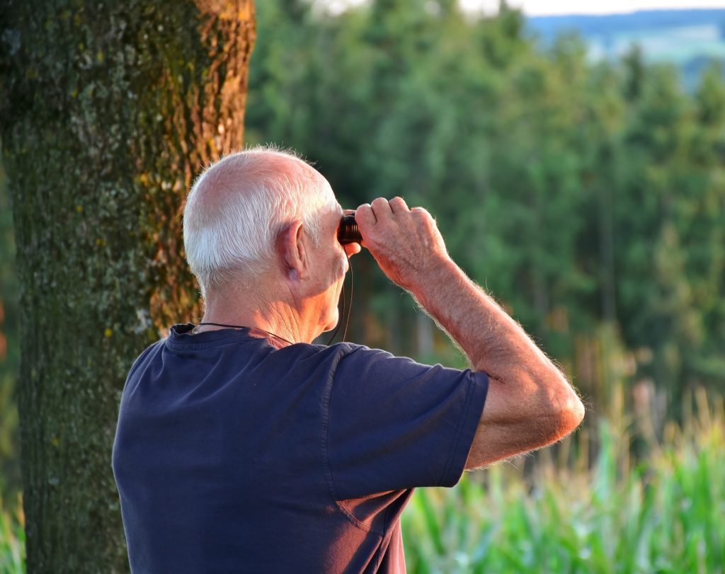 Homme âgé seul qui regarde au loin avec des jumelles dans la nature